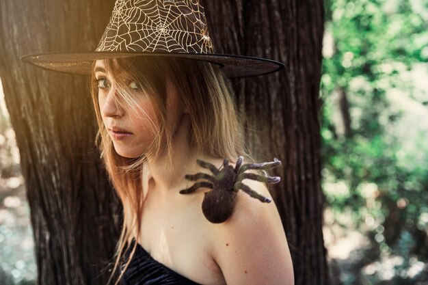 Hermosa mujer con sombrero con araña decorativa en hombro mirando a cámara