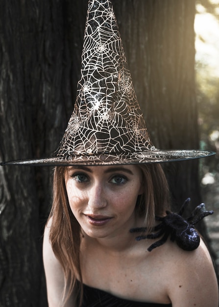 Hermosa mujer con sombrero de bruja mirando la cámara con araña decorativa sentado en el hombro