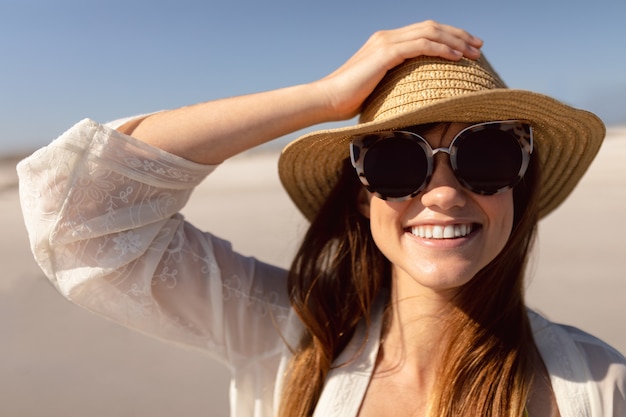 Hermosa mujer con sombrero y gafas de sol de pie en la playa bajo el sol