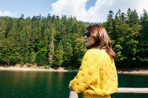 Hermosa mujer sonriendo, disfrutando de la vista de las montañas, el lago y el bosque