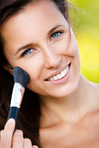 Hermosa mujer sonriente con pincel de maquillaje