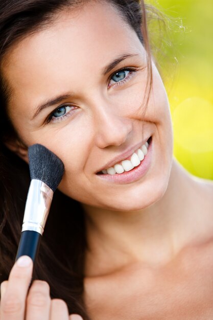 Hermosa mujer sonriente con pincel de maquillaje