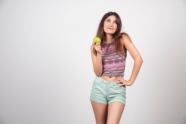 Hermosa mujer sonriente posando con una manzana en ropa de verano.