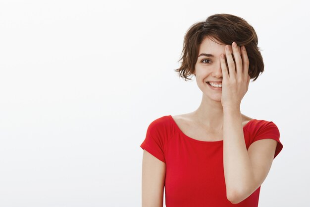 Hermosa mujer sonriente que parece feliz, cubre la mitad de la cara con la palma