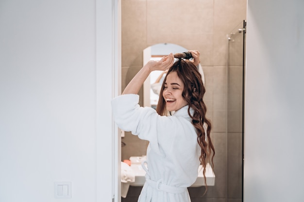 Hermosa mujer sonriente rizar el cabello largo con rizador