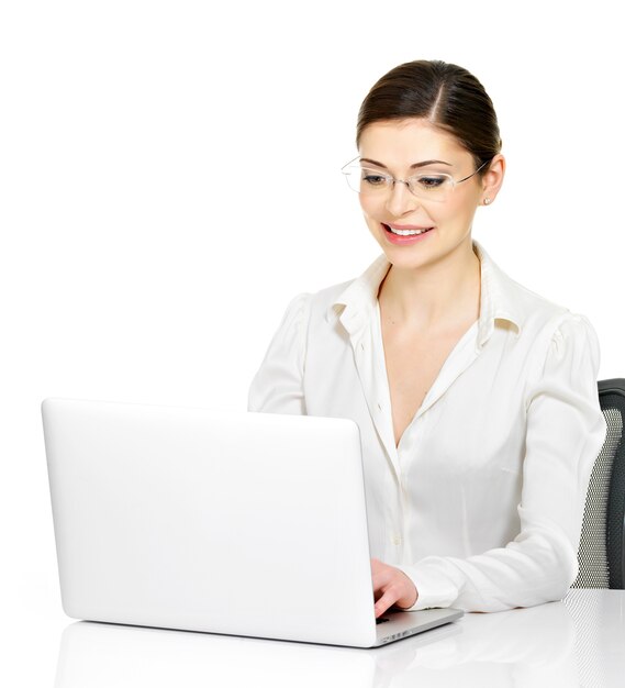 Hermosa mujer sonriente se sienta desde la mesa de thÑƒ con laptop en camisa blanca - aislado en blanco.