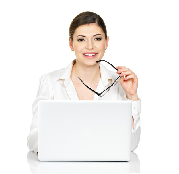 Hermosa mujer sonriente se sienta desde la mesa de thÑƒ con laptop en camisa blanca - aislado en blanco.