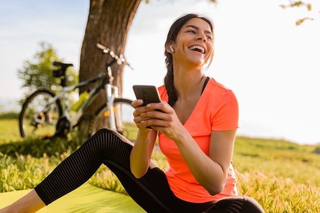 Hermosa mujer sonriente sosteniendo el teléfono haciendo deporte en la mañana en el parque