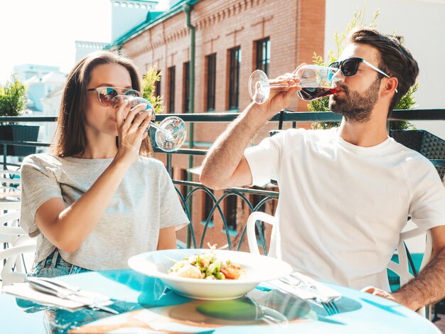 Hermosa mujer sonriente y su guapo novio Familia feliz y alegre Pareja animando con copas de vino tinto en su cita en el restaurante Ellos beben alcohol en el café de la terraza en la calle