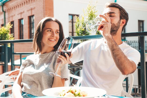 Hermosa mujer sonriente y su guapo novio Familia feliz y alegre Pareja animando con copas de vino tinto en su cita en el restaurante Ellos beben alcohol en el café de la terraza en la calle