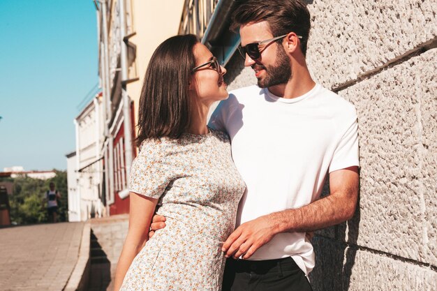 Hermosa mujer sonriente y su guapo novio Mujer con ropa casual de verano Familia feliz y alegre Mujer divirtiéndose Pareja posando en el fondo de la calle con gafas de sol Abrazándose unos a otros