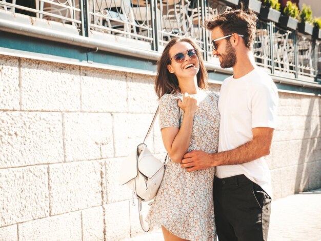 Hermosa mujer sonriente y su guapo novio Mujer con ropa casual de verano Familia feliz y alegre Mujer divirtiéndose Pareja posando en el fondo de la calle con gafas de sol Abrazándose unos a otros