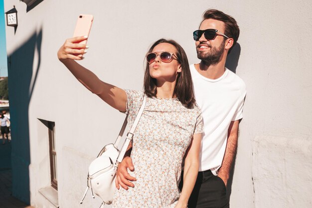 Hermosa mujer sonriente y su guapo novio Mujer con ropa informal de verano Familia feliz y alegre Mujer divirtiéndose Pareja posando en la calle cerca de la pared Abrazándose unos a otros Tomando selfie