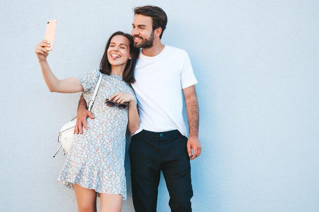 Hermosa mujer sonriente y su guapo novio Mujer con ropa informal de verano Familia feliz y alegre Mujer divirtiéndose Pareja posando en la calle cerca de la pared Abrazándose unos a otros Tomando selfie