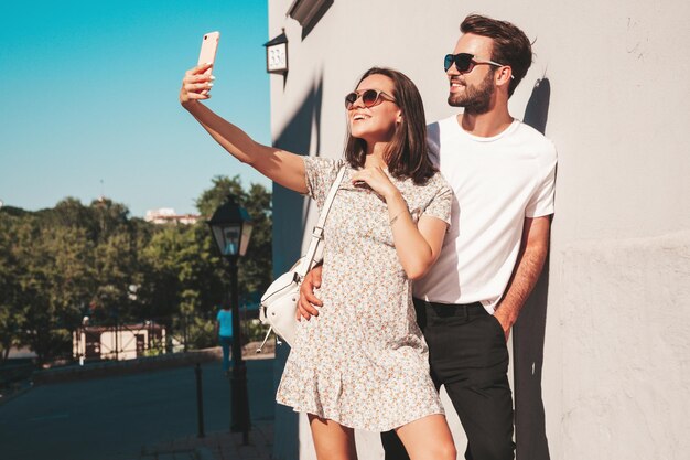 Hermosa mujer sonriente y su guapo novio Mujer con ropa informal de verano Familia feliz y alegre Mujer divirtiéndose Pareja posando en el fondo de la calle con gafas de solTomando fotos selfie