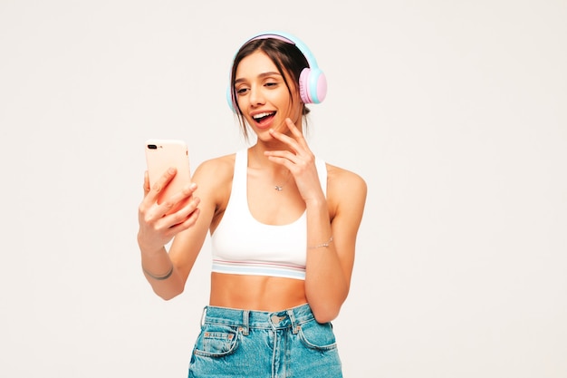 Hermosa mujer sonriente vestida con ropa de jeans. modelo despreocupado escuchando música en auriculares inalámbricos