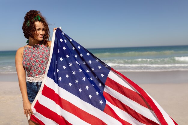 Hermosa mujer sosteniendo la bandera americana en la playa en el sunshifcane