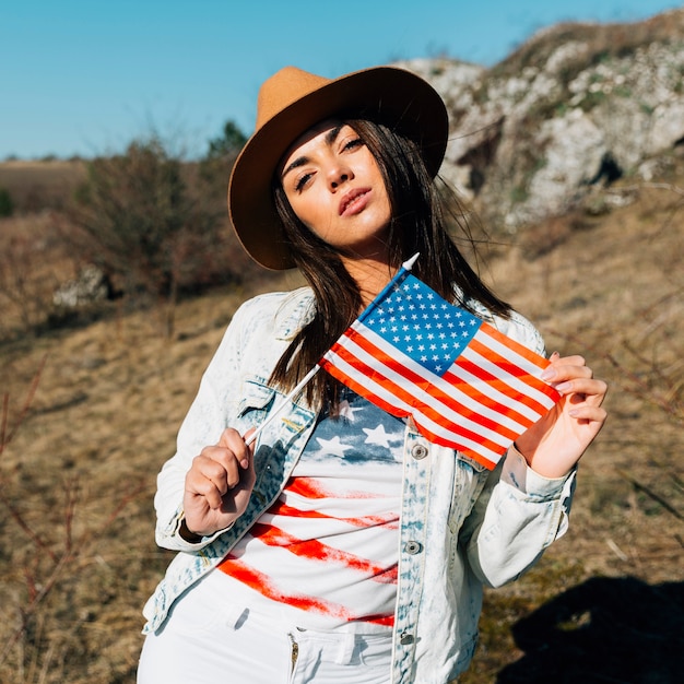 Hermosa mujer sosteniendo bandera estadounidense en la naturaleza