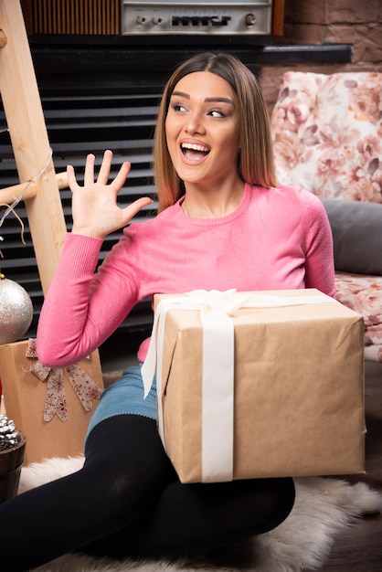 Hermosa mujer sosteniendo caja de regalo con expresión feliz en casa
