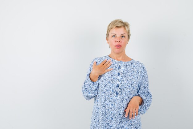 Hermosa mujer sosteniendo la mano en el pecho en blusa estampada y mirando emocional, vista frontal.