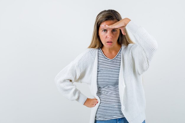 Hermosa mujer sosteniendo la mano sobre la cabeza en chaqueta, camiseta y mirando perplejo. vista frontal.