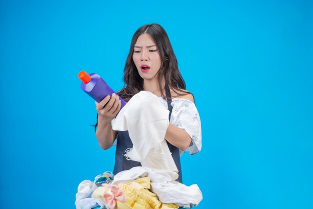 Una hermosa mujer sosteniendo un paño y detergente líquido preparado para lavar en azul