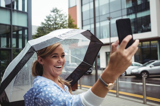Hermosa mujer sosteniendo paraguas mientras toma selfie