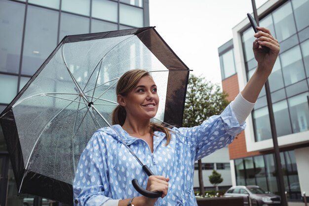 Hermosa mujer sosteniendo paraguas mientras toma selfie