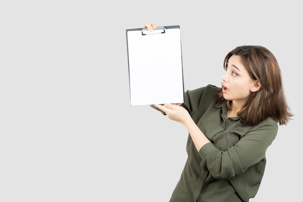 Hermosa mujer sosteniendo el portapapeles y mirándolo sobre una pared blanca. Foto de alta calidad