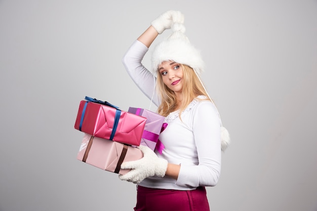 Hermosa mujer sosteniendo regalos de Navidad en la pared gris.