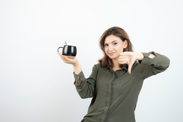 Hermosa mujer sosteniendo una taza de café y dando pulgares hacia abajo. foto de alta calidad