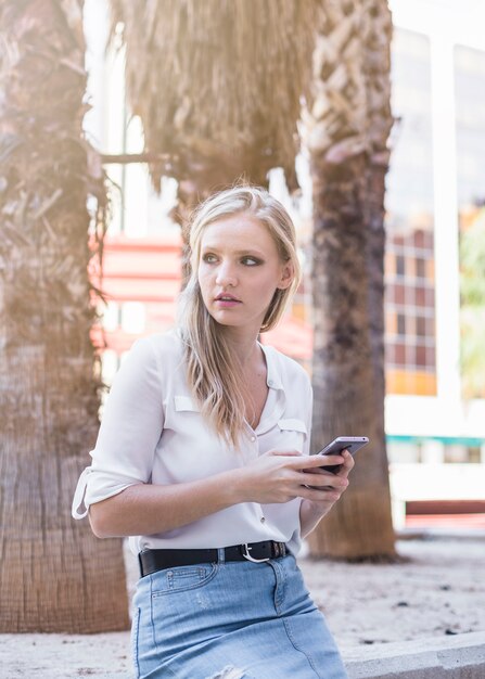 Hermosa mujer sosteniendo teléfono celular apartar la mirada