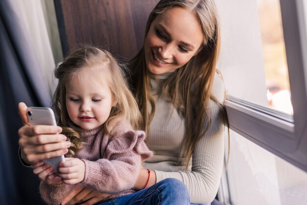 Hermosa mujer y su pequeña hija linda están haciendo selfie usando un teléfono inteligente