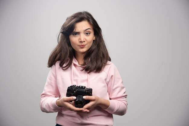 Hermosa mujer en sudadera rosa posando con cámara.