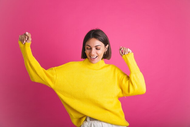 Hermosa mujer en suéter amarillo brillante aislado en rosa feliz emocionado bailando sonrisa en movimiento