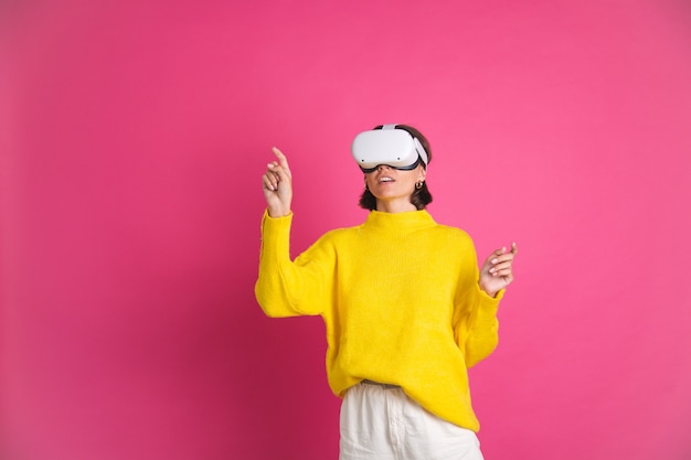 Hermosa mujer en suéter amarillo brillante en rosa en gafas de realidad virtual punto feliz a la izquierda con el dedo al espacio vacío