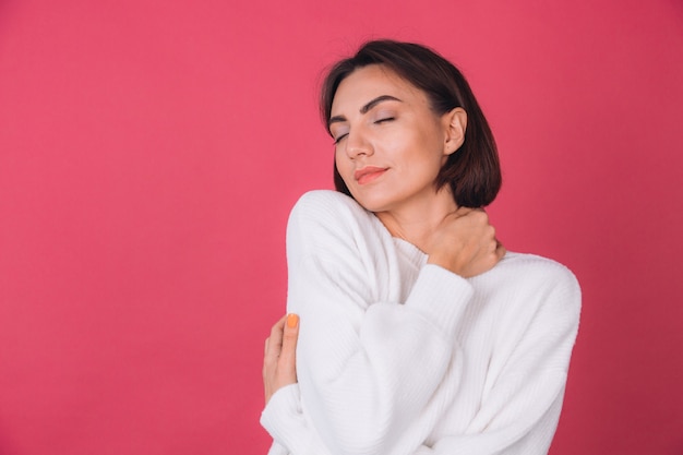 Hermosa mujer en suéter blanco casual, concepto de amor, tomados de la mano cruzados abrazándose a sí misma con los ojos cerrados