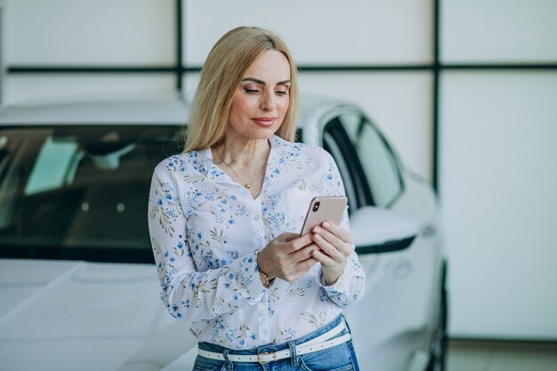 Hermosa mujer con teléfono en la sala de exposición de automóviles