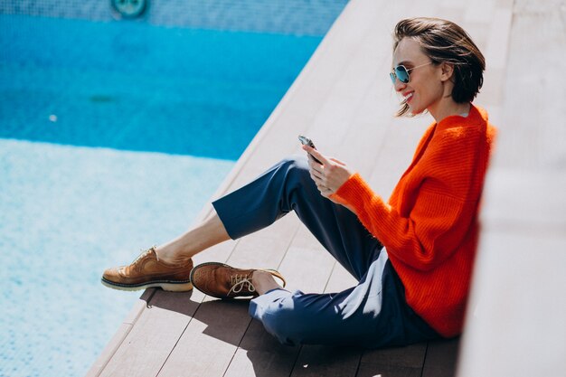 Hermosa mujer con teléfono sentado junto a la piscina