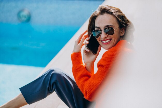 Hermosa mujer con teléfono sentado junto a la piscina