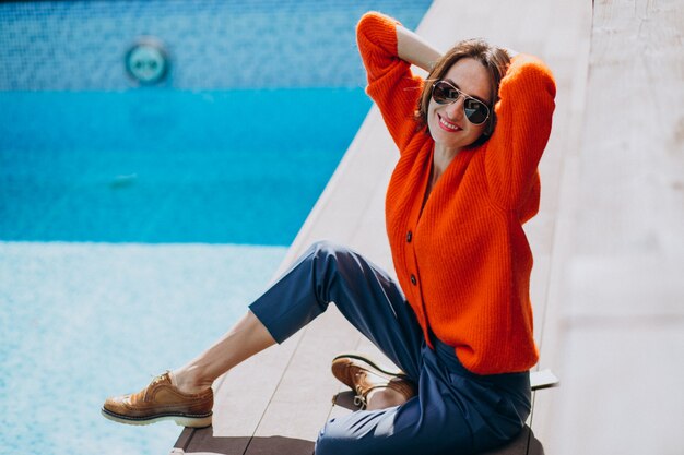 Hermosa mujer con teléfono sentado junto a la piscina