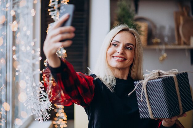 Hermosa mujer con teléfono por ventana en Navidad