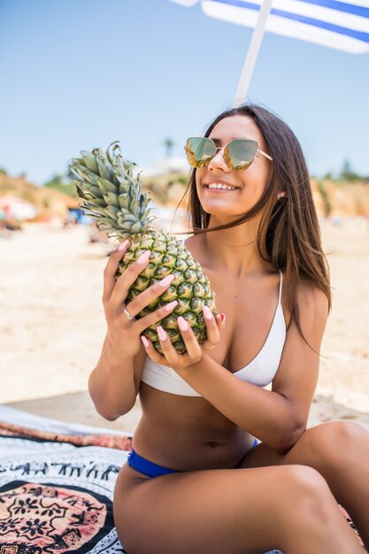 Hermosa mujer tiene piña en manos de una playa tropical relajante. Hermosa modelo de mujer con frutas tropicales en sus manos