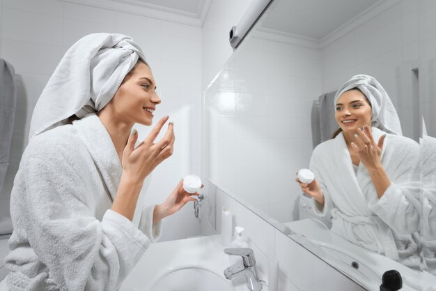 Hermosa mujer con toalla blanca después de la ducha haciendo maquillaje