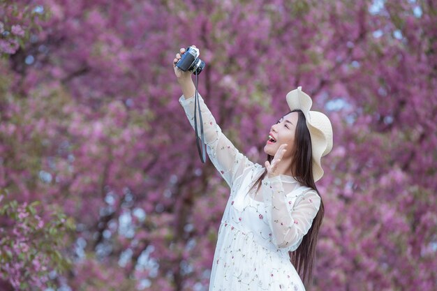 Una hermosa mujer toma una foto con una cámara de cine en el jardín de flores de Sakura.