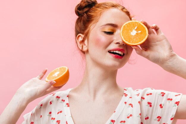 Hermosa mujer en top blanco con estampado de cereza posando con naranjas sobre fondo aislado.