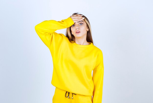 Hermosa mujer en traje amarillo con dolor de cabeza sobre pared blanca