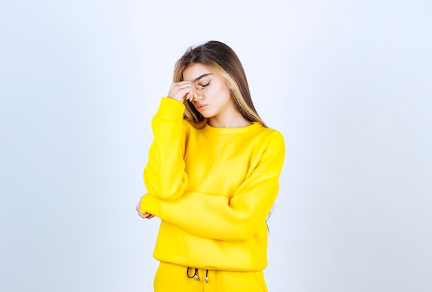 Hermosa mujer en traje amarillo con dolor de cabeza sobre pared blanca