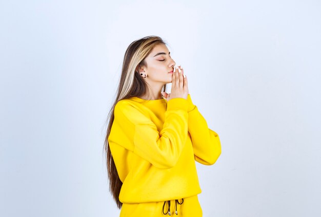 Hermosa mujer en traje amarillo de pie y posando sobre pared blanca