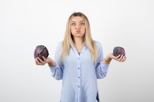 Hermosa mujer en traje azul con repollo morado sobre pared blanca.